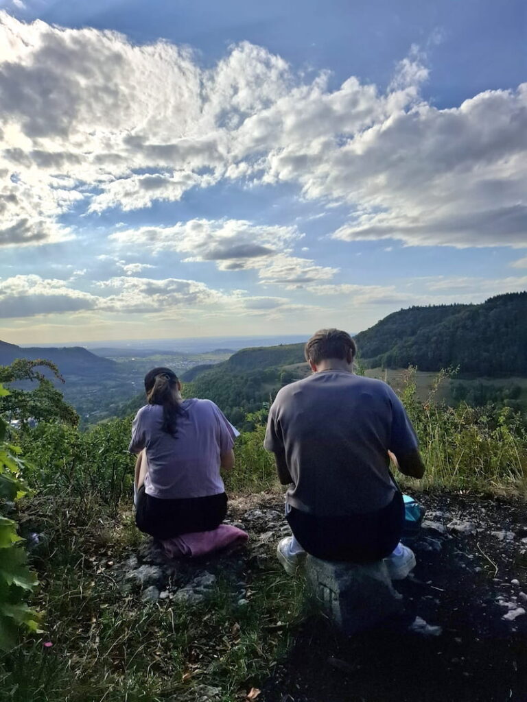 Zwei Menschen sitzen auf aussichtsreichem Felsen im Wald und schreiben
